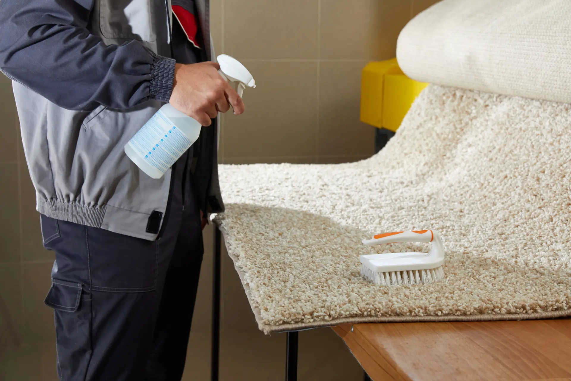 Man Spraying Detergent On Grey Carpet To Remove Stain in professional cleaning service